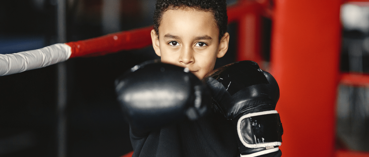 A young boy poses holding up his boxing gloves.
