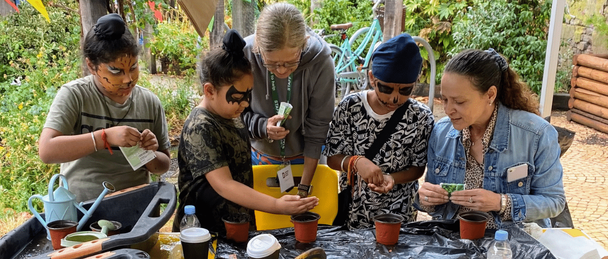 Two women are helping a group of young boys to plant seeds in a pot