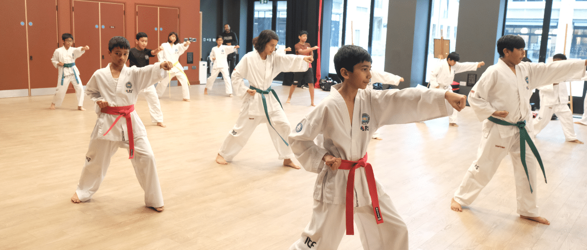 A group of young boys and girls practising punching techniques together during a Taekwondo class at Feldy Community Space