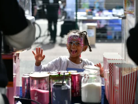 A young girl with a painted face waves at the camera at the Teviot Festival