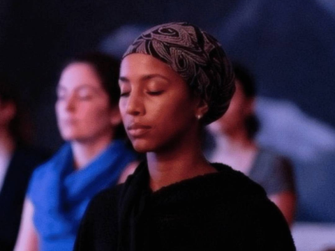 A young woman looks peaceful as she meditates in a wellness class with her eyes closed