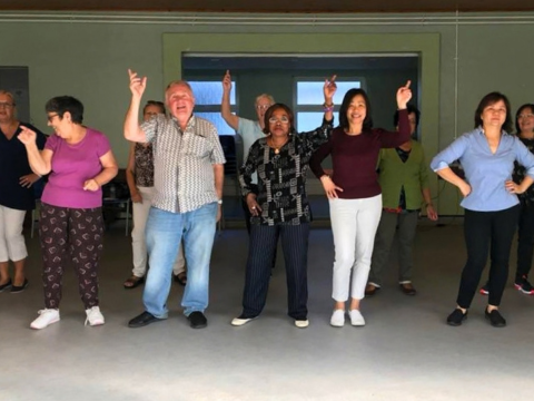 A group of men and women are taking part in a gentle Good Moves exercise session